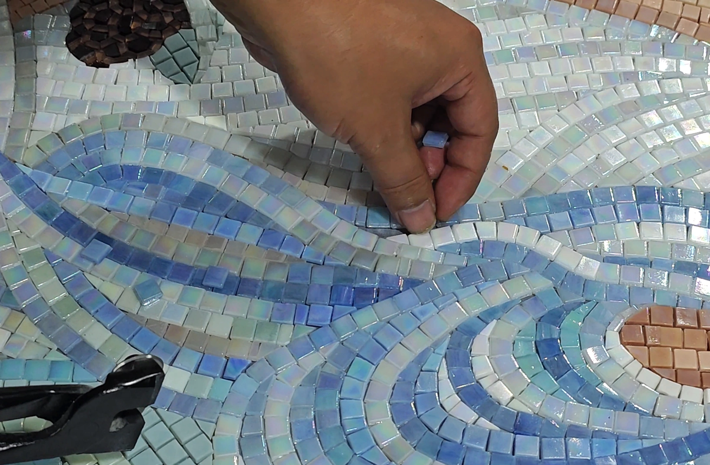 Artisan placing an individual mosaic piece along a curved design